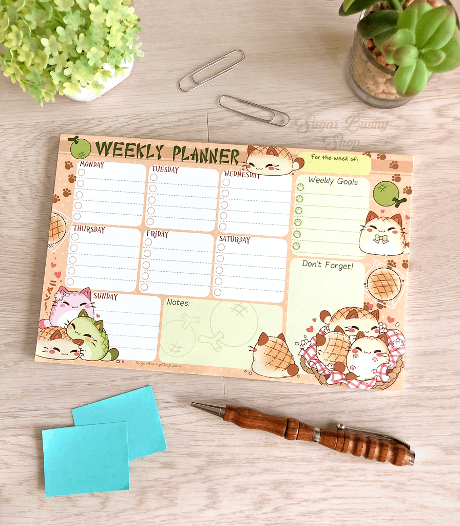 A photo of a weekly planner notepad on a table with plants, the design featuring Nyanpan the bread cat in various poses with task sections for each day of the week, as well as extra notes and goals.
