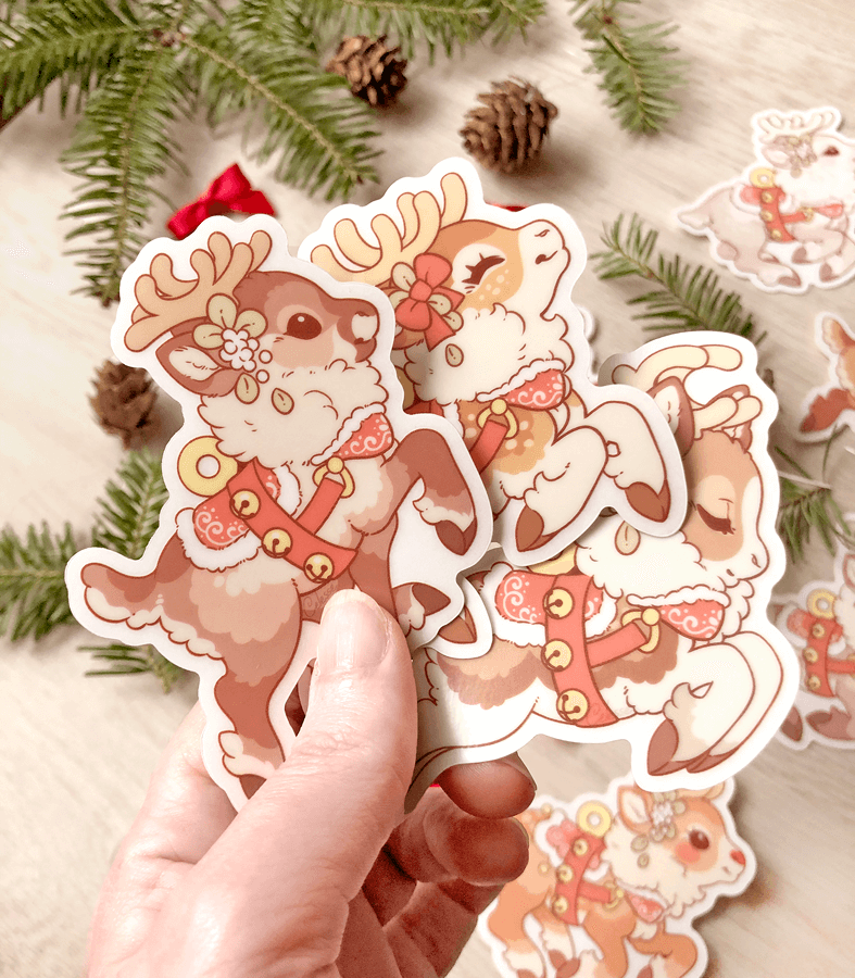 A photo of a hand holding three vinyl stickers featuring artwork of different designs for Santa&